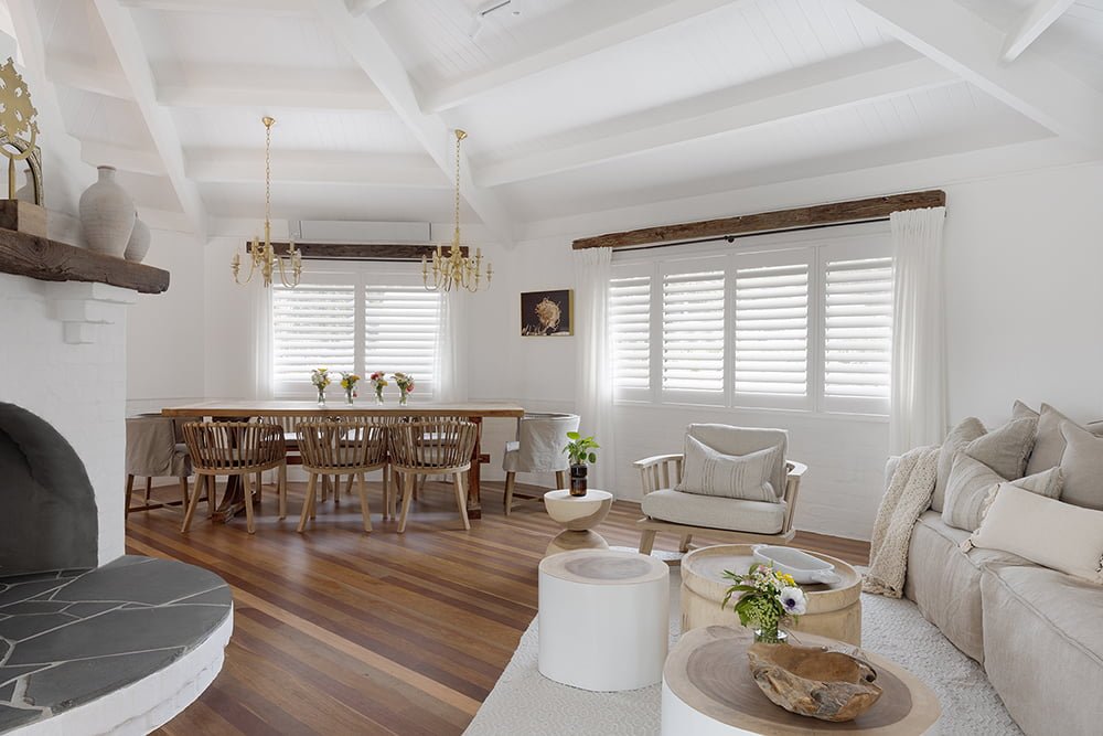 Bright and spacious living and dining area featuring Norman’s Shutters, providing light control and privacy while enhancing the room’s natural elegance. The space is styled with warm wood accents, soft neutral tones, and rustic touches, creating a cozy yet sophisticated atmosphere.