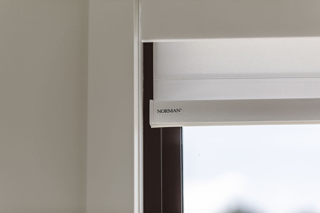 A close-up of Norman's PerfectSheer Shades, showcasing the fine details of the fabric and the subtle Norman logo on the shade's bottom edge. The design reflects the brand's commitment to quality and style, blending seamlessly with the window frame.