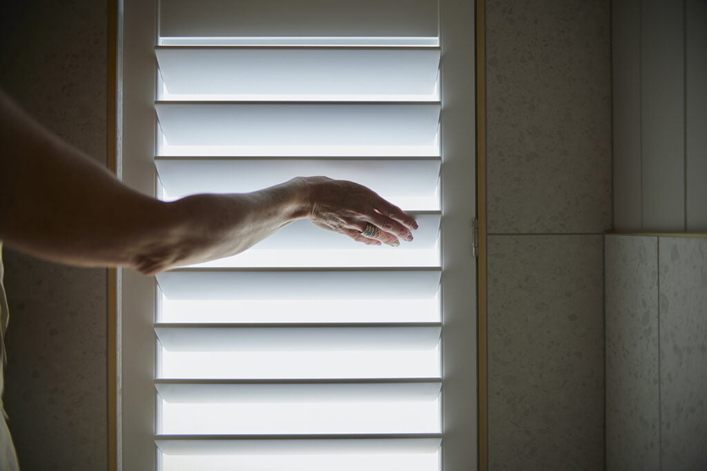 A close-up of a hand adjusting Norman’s Woodlore Plus Waterproof Shutters, showcasing their durable design and smooth operation. Perfect for moisture-prone spaces, these shutters combine functionality with a sleek aesthetic.